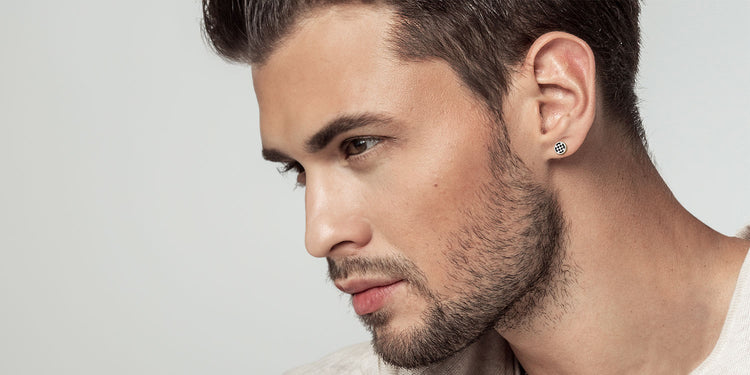 Junger Mann mit Bart im Profil trägt modernen silbernen Ohrstecker mit Muster