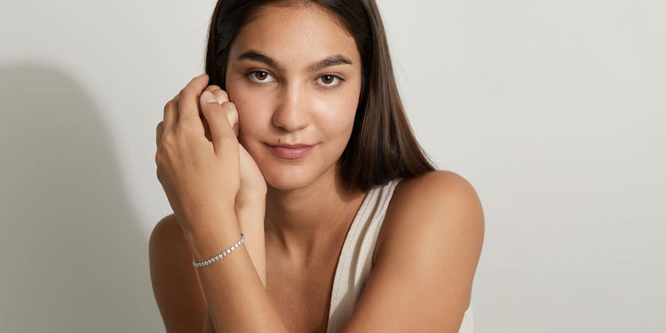 unge Frau trägt ein zartes silbernes Tennis-Armband, posiert elegant vor weißem Hintergrund