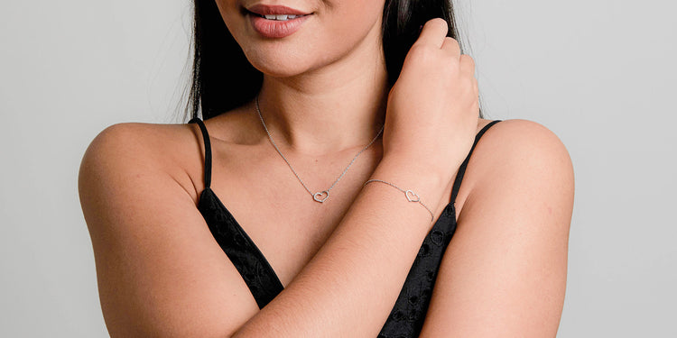 Frau trägt elegante Goldkette mit Herzanhänger und passendes Armband, schwarzes Oberteil