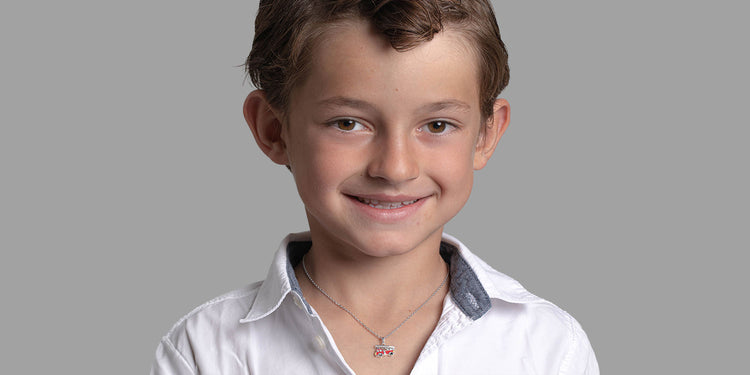 Lächelnder Junge mit braunen Haaren in weißem Hemd trägt silberne Halskette mit buntem Anhänger 