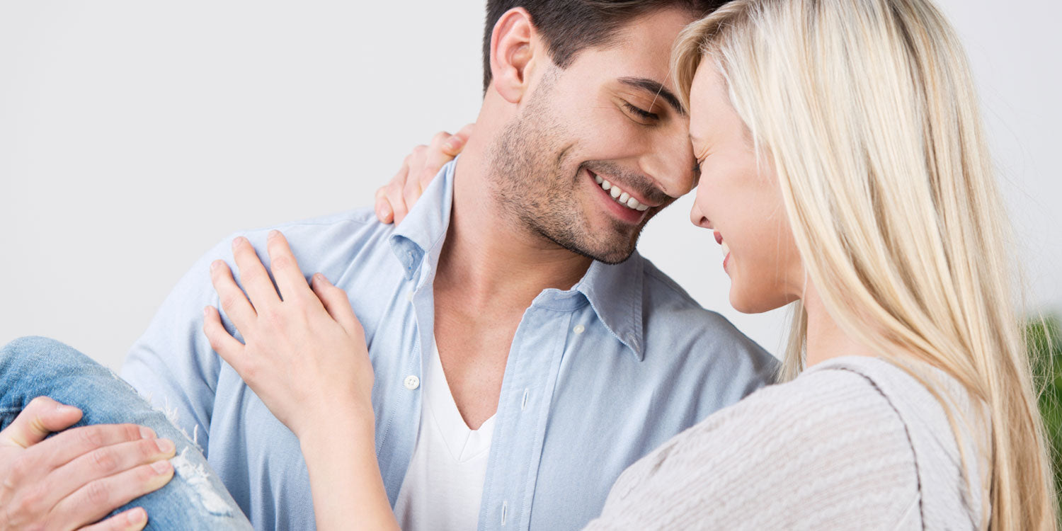 Glückliches Paar in inniger Umarmung - beide tragen Ringe, Mann in hellblauem Hemd, blonde Frau in beigem Pullover