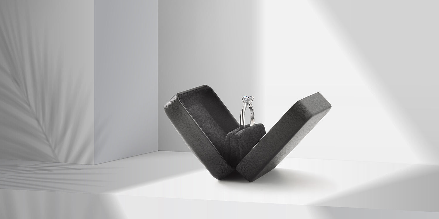 Eleganter Solitär-Verlobungsring aus Weißgold mit Diamant, präsentiert in einem modernen schwarzen Ringetui mit raffinierter Ring-Halterung vor minimalistischem weißem Hintergrund