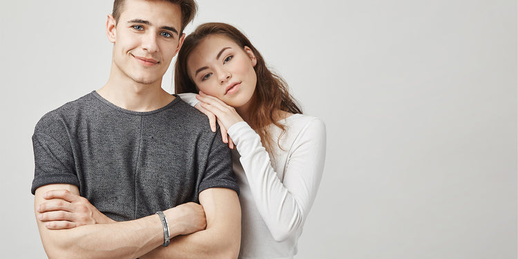 Junges Paar - Mann trägt schwarzes Gravurarmband, Frau lehnt sich an seine Schulter