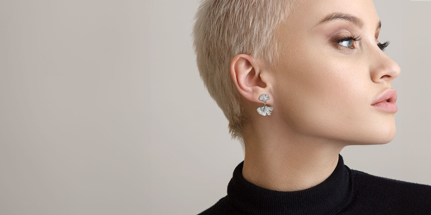 Blonde Frau mit kurzem Pixie-Cut in schwarzem Pullover trägt silberne Ohrringe mit Blatt-Design 