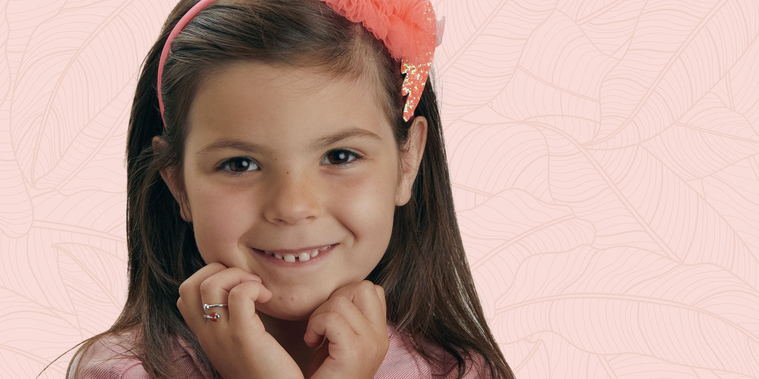 Lächelndes Mädchen mit Haarreif trägt bunten Kinderring vor rosa Hintergrund